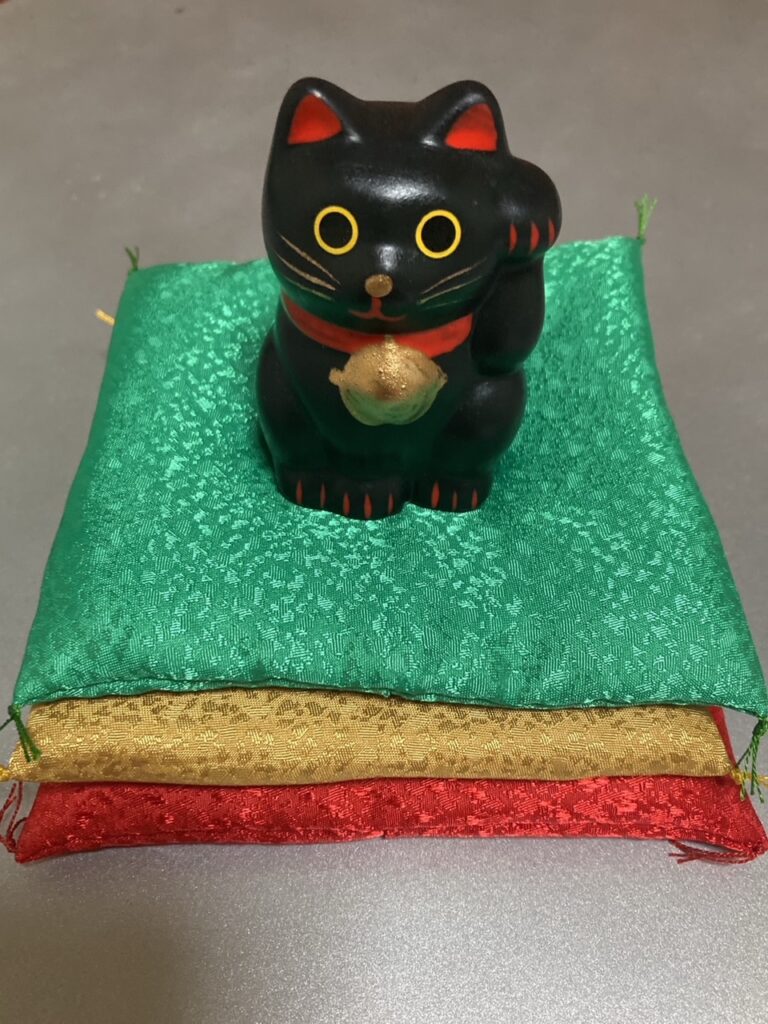 座布団（緑色・金色・赤色）にのった黒招き猫